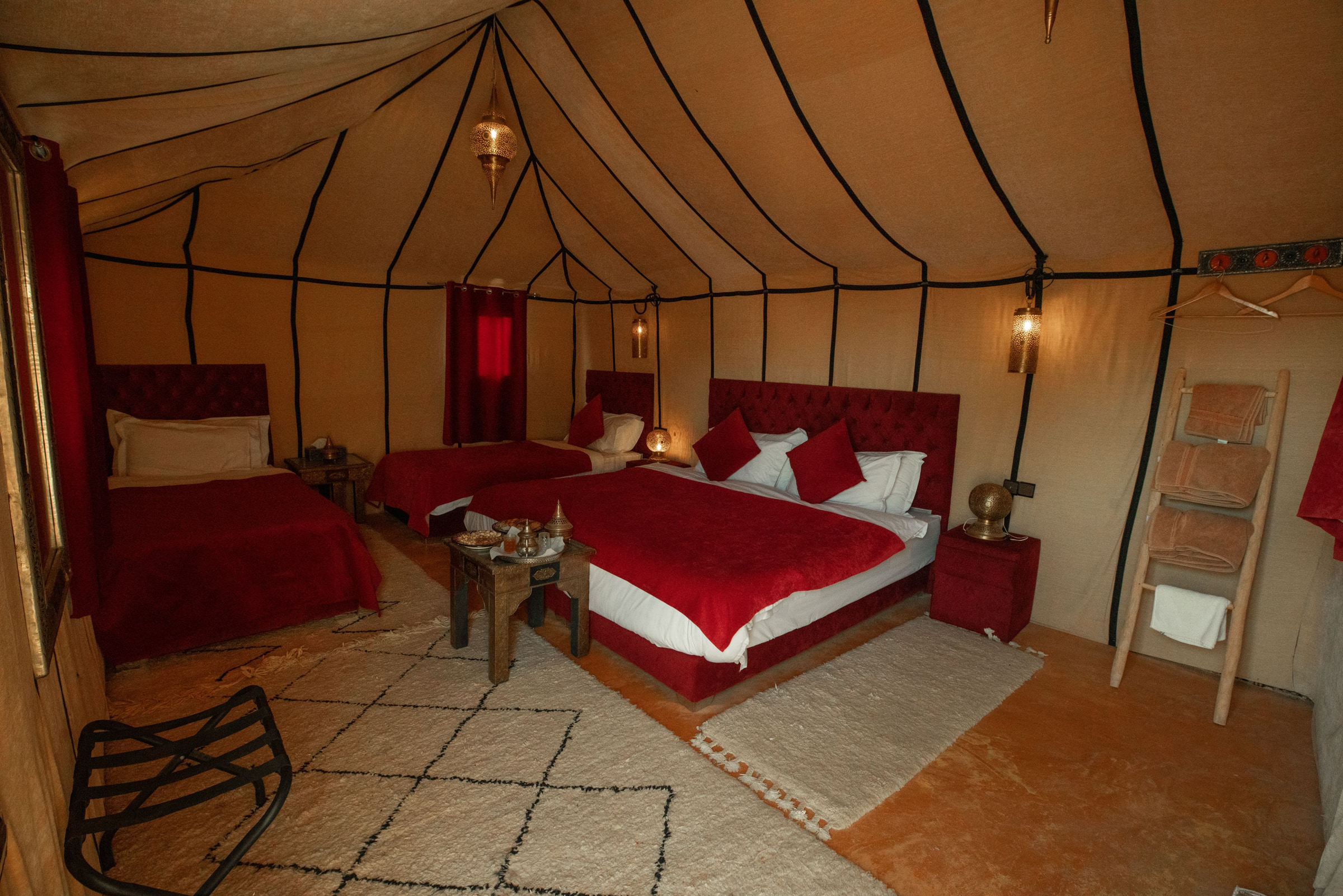 Luxury tent interior with deep-red tufted velvet beds, brass tea service and hand-knotted Berber rugs