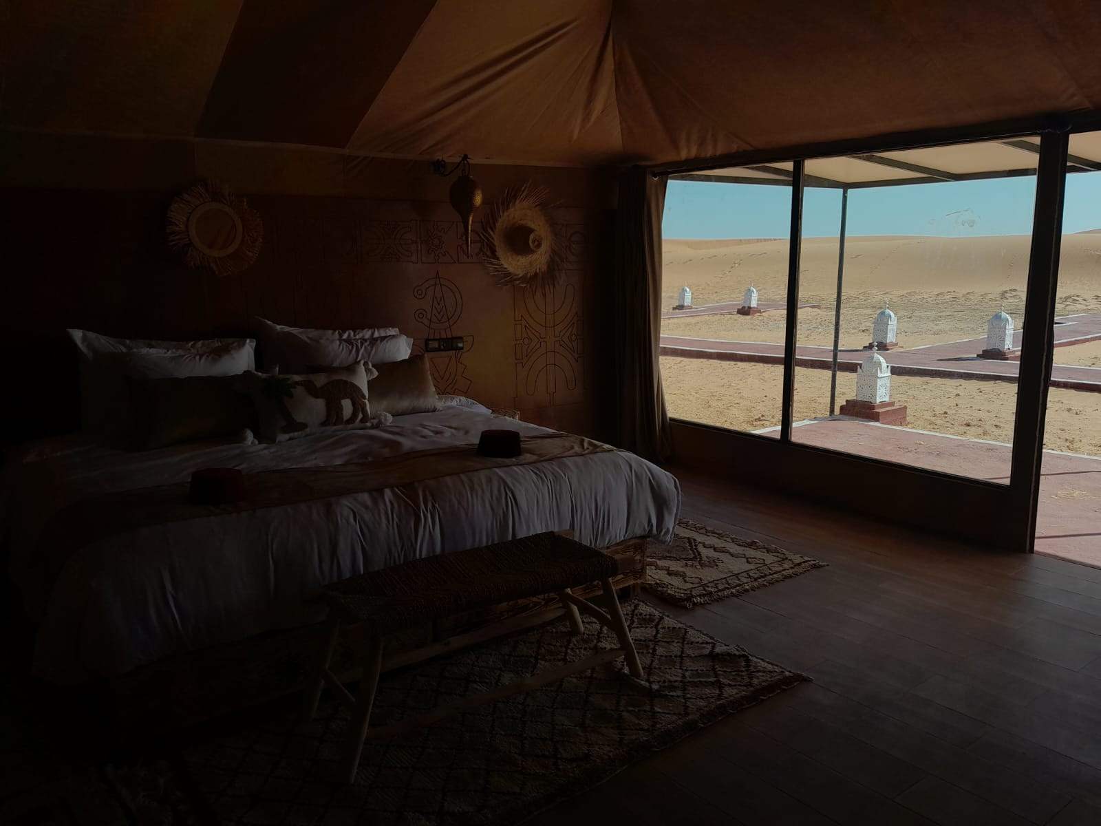 Silhouetted tent bedroom overlooking golden Erg Chebbi dunes through a floor-to-ceiling glass door