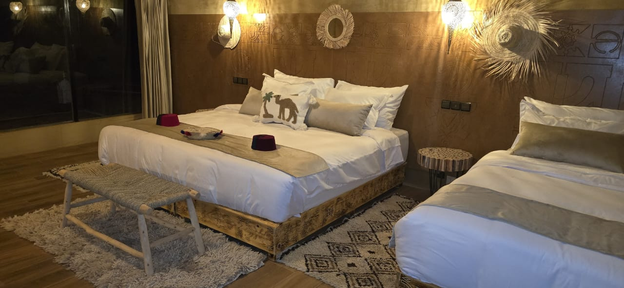 Carved wooden bed frame dressed in white linens beneath Moroccan mirrors and pendant lanterns at night