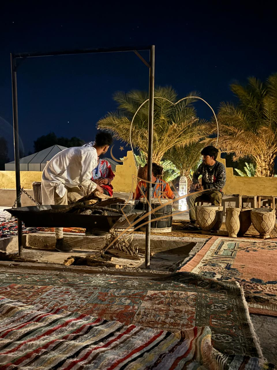 Staff preparing traditional drums beside the fire pit under a heart-shaped arch and illuminated palms
